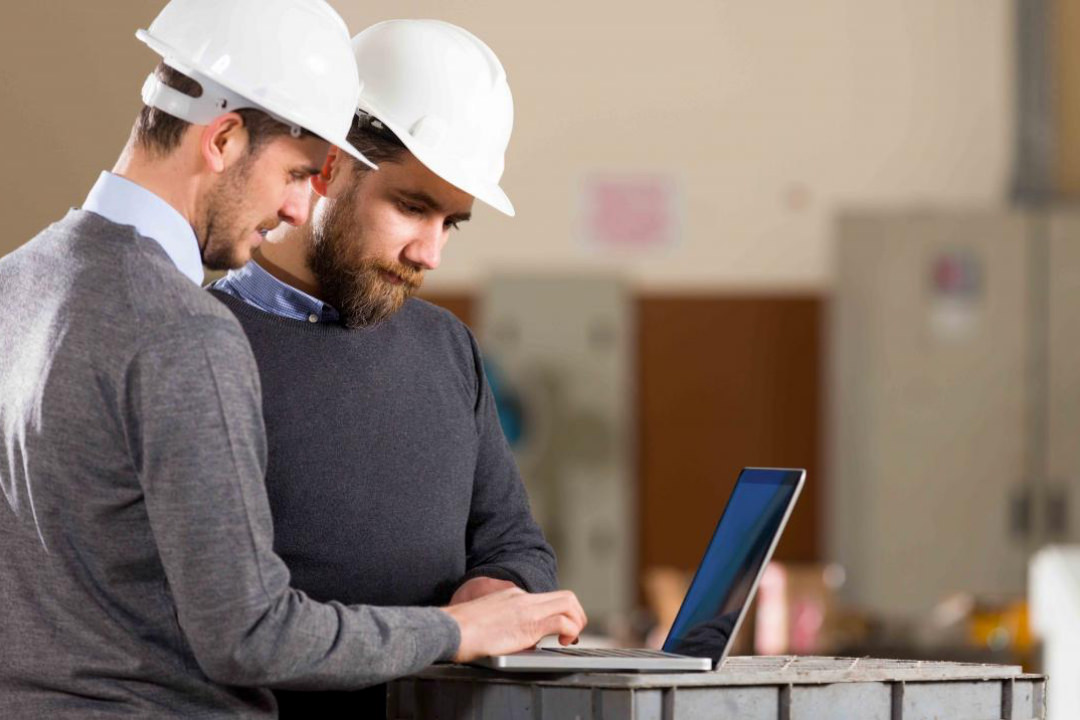 Image of two engineers on a construction site with hard hats on deep diving into figures on a laptop