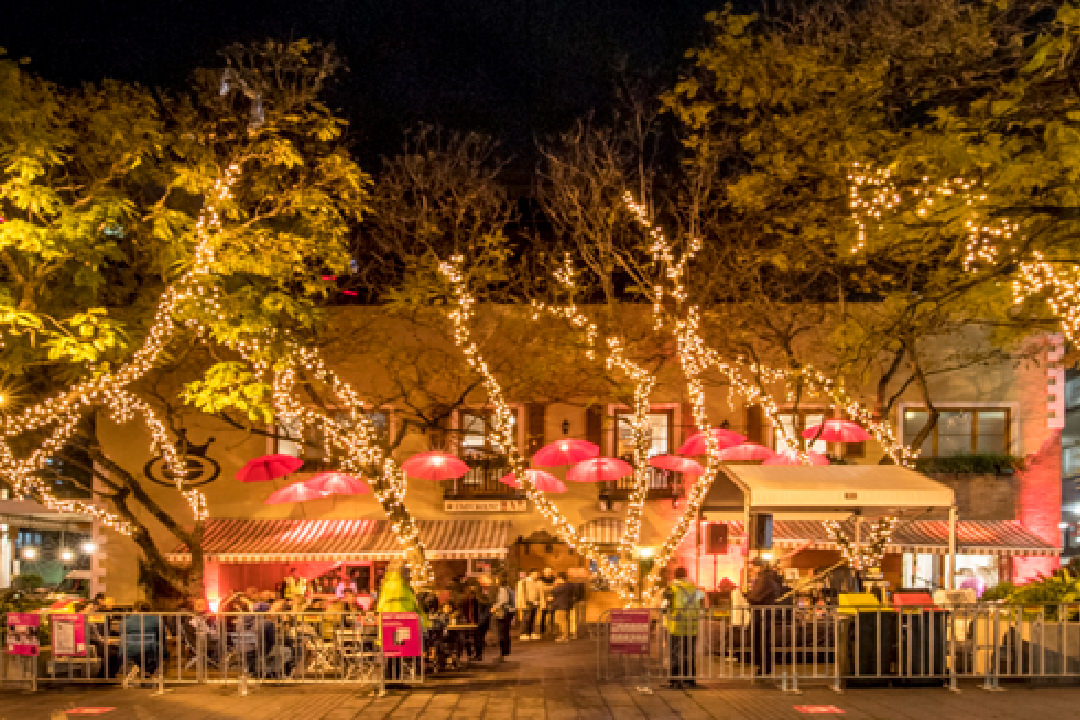 Image of the Emporium Restaurant during the Parramatta Lanes Festival in October. The restaurant is surround with large willow trees strung with lights. Umbrellas have also been hung around the restaurant exterior and in the trees. 