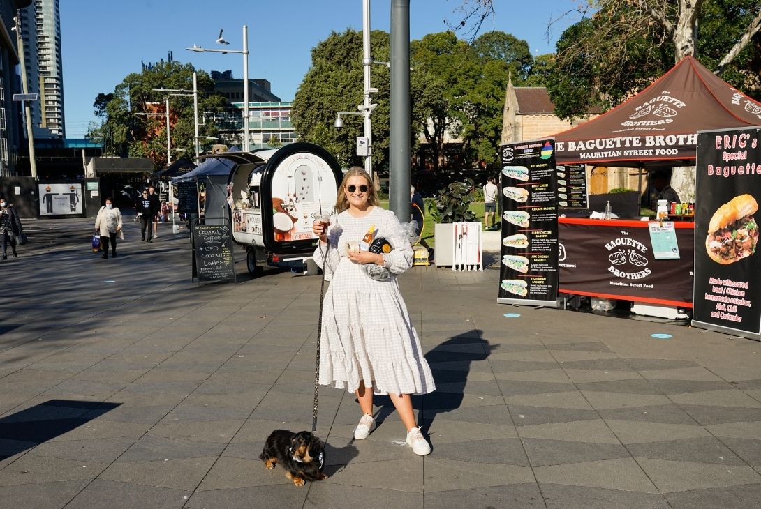 woman standing at farmers markets, with her sausage dog on a leash