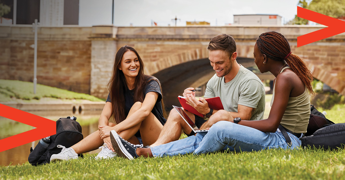 three students sitting on grass talking in front of lennox bridge