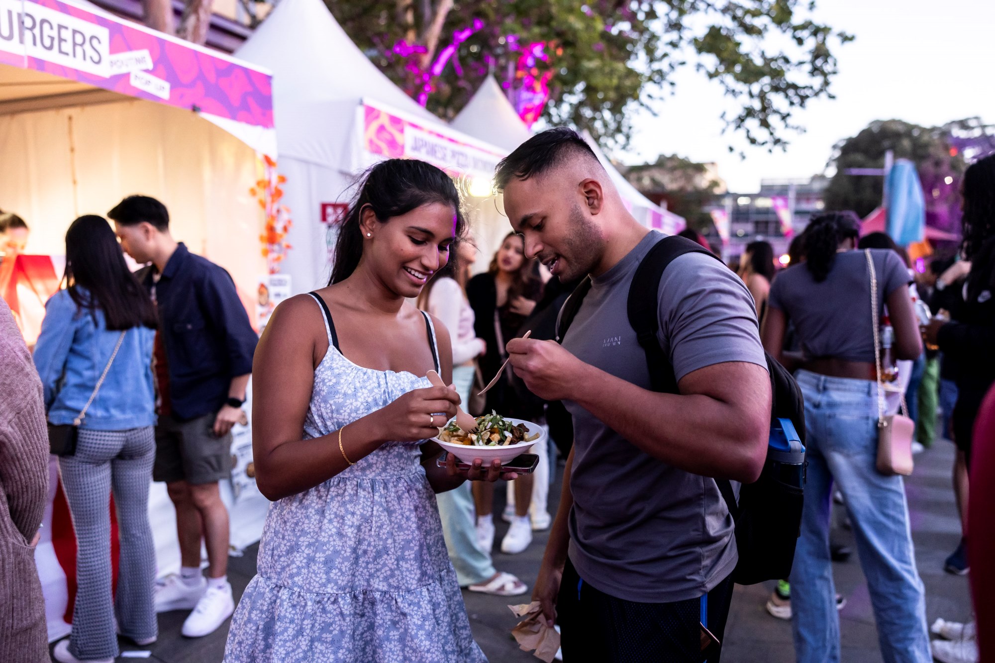 Two people standing at a good tent eating