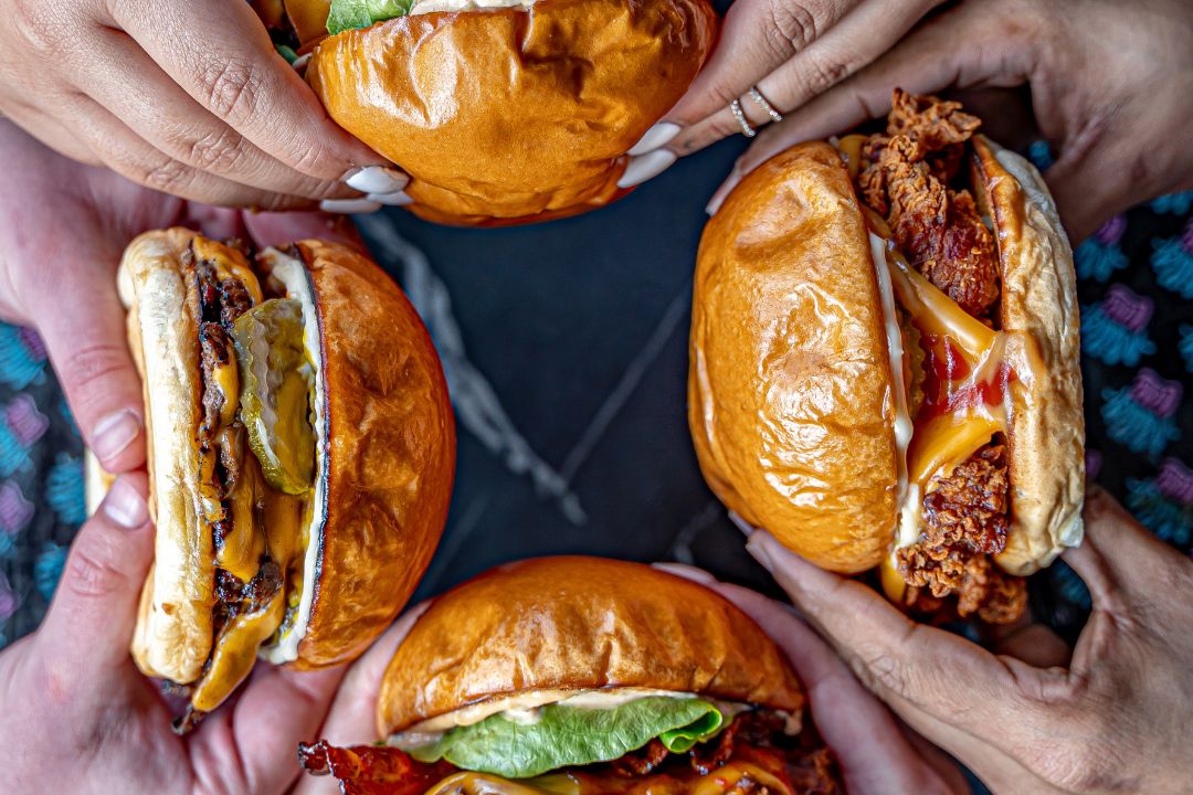 four hands holding burgers