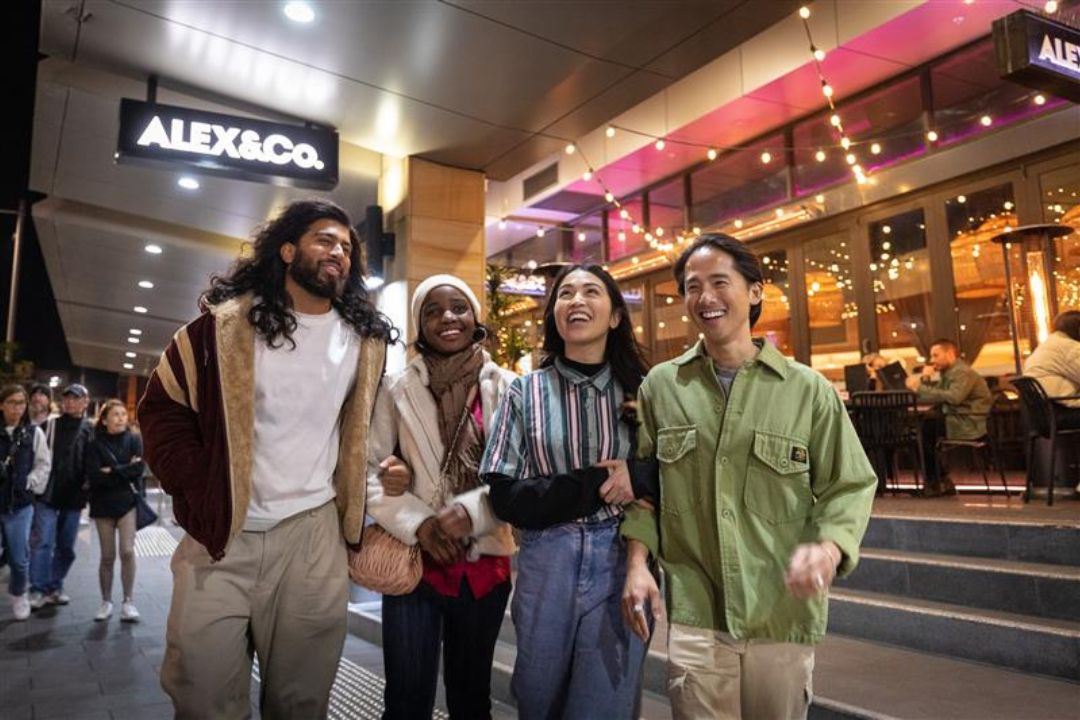 4 people walking down a street smiling at each other