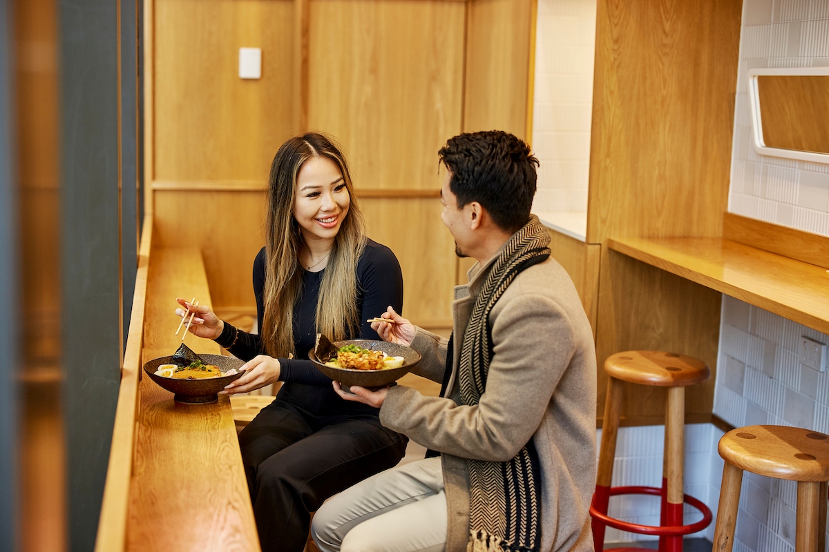 Two people sit down to eat ramen together in a restaurant featuring wooden furniture.