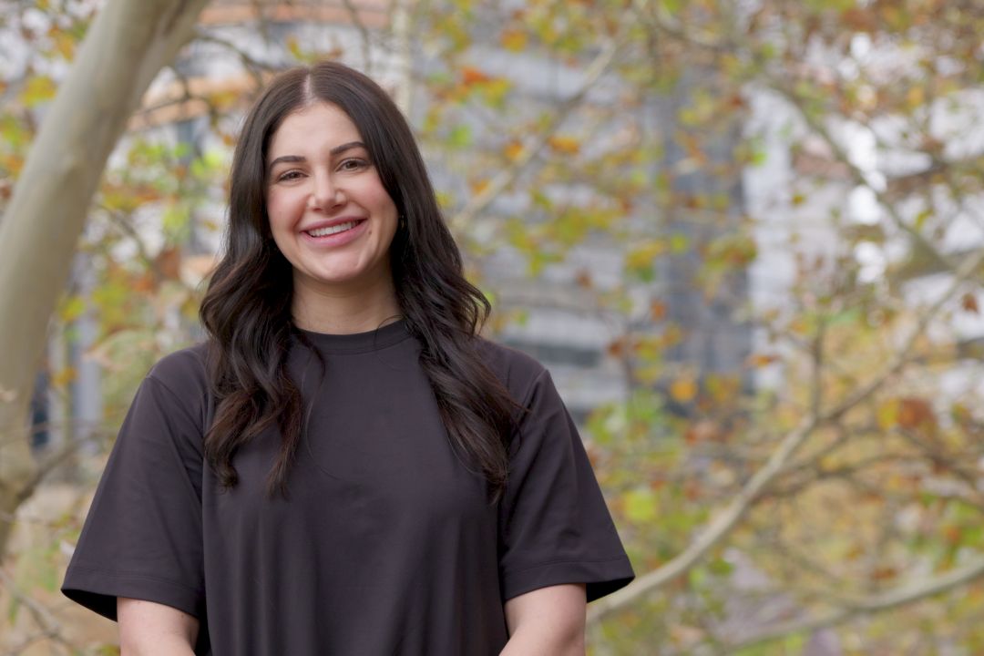 Brunette woman in black shirt standing in front of large tree with leaves turning orange