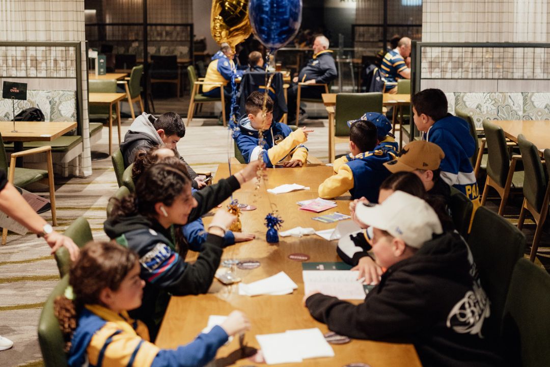 Group of children sitting at large wooden table in yellow and blue shirts