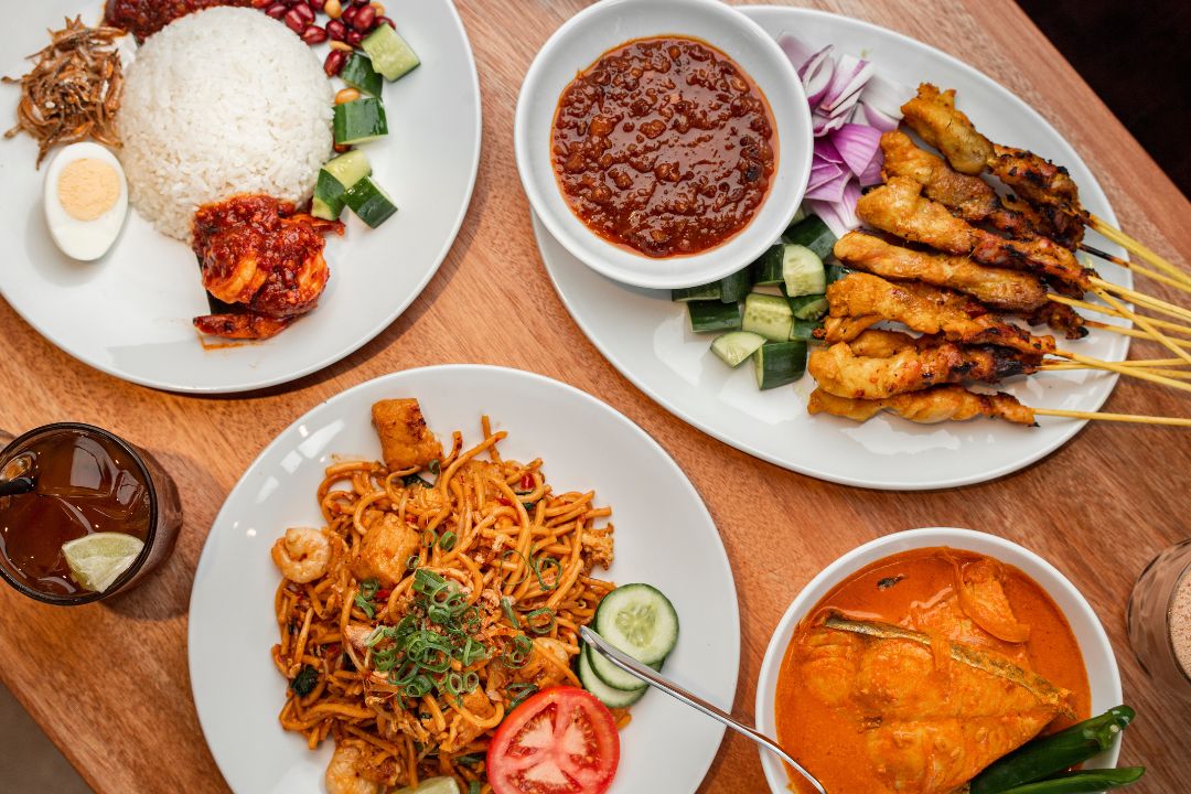 Table covered in plates of food like skewers & dipping sauce, rice & meat dishes