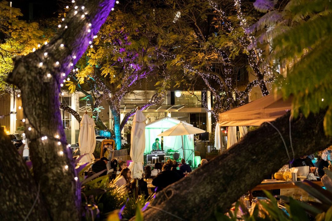 People sitting in courtyard watching man play guitar on stage at night time