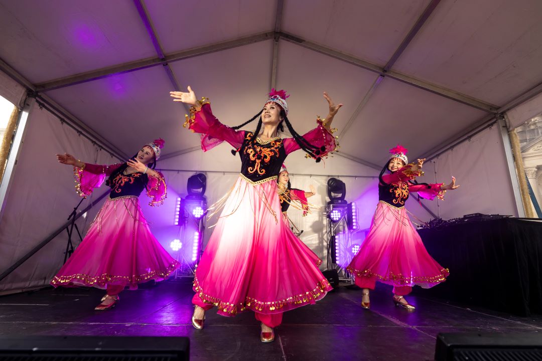 3 dances in long white and pink dresses wearing traditional asia headwear, dancing on a stage