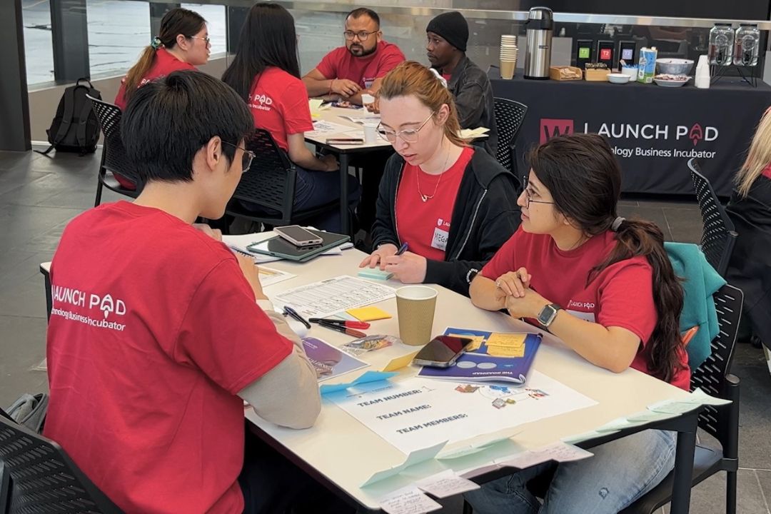A group of people wearing red shirts are engaged in a collaborative activity at tables with papers and art supplies. The mood is focused and creative.