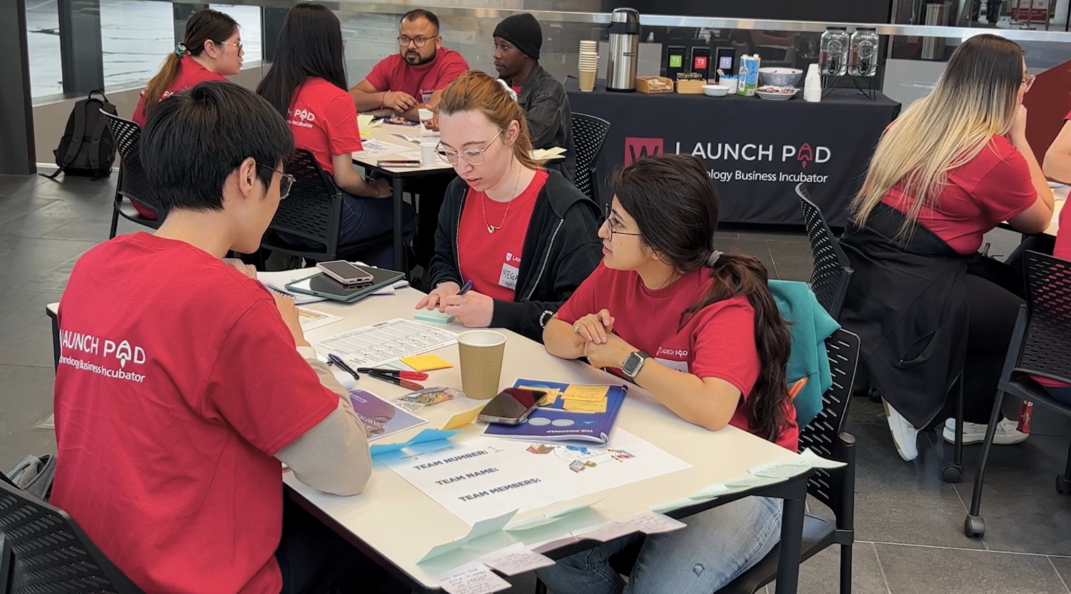 A group of people wearing red shirts are engaged in a collaborative activity at tables with papers and art supplies. The mood is focused and creative.