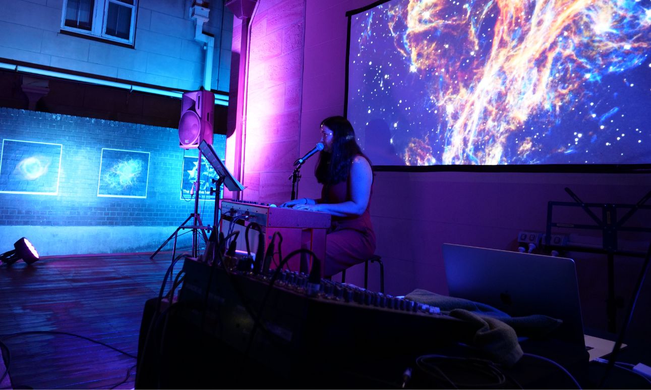 A vibrant indoor scene with a DJ playing music. Neon blue and purple lights illuminate the space, casting dynamic shadows. A projection displays abstract visuals.
