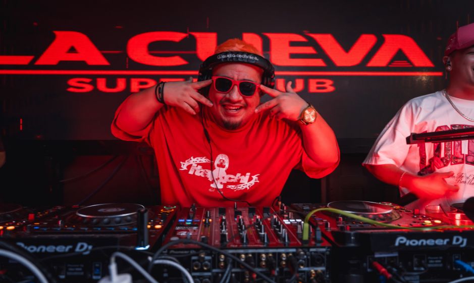 DJ in vibrant red attire performs energetically behind a mixing console at La Cheva nightclub. The scene is lively, with dynamic lighting and a party vibe.