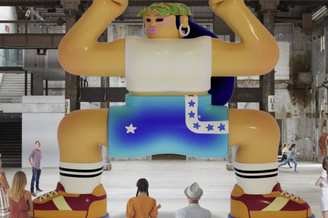A giant inflatable cartoon character with a muscular build, wearing blue shorts, is displayed indoors. People gather around, observing and taking photos.