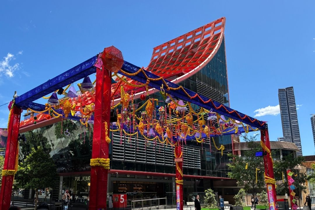 A vibrant Chinese archway adorned with colorful lanterns under a clear blue sky. Modern skyscrapers rise in the background, blending tradition and urban life.