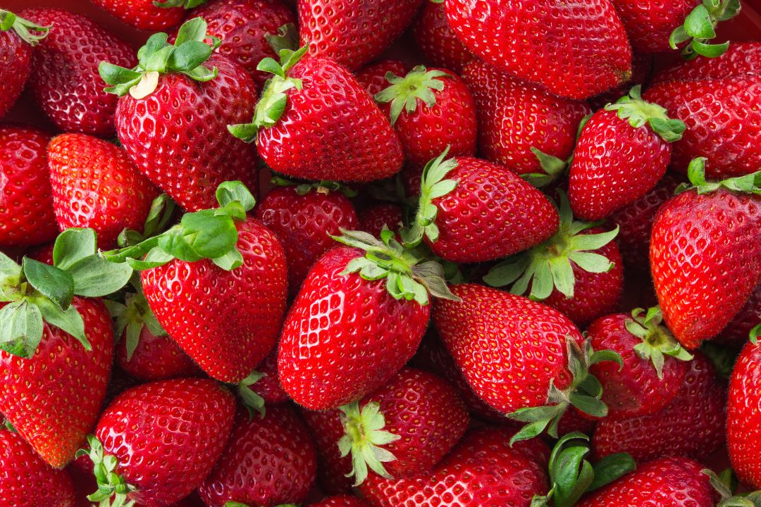 A cluster of ripe, red strawberries with vivid green leaves, showcasing their juicy texture and freshness. The image conveys a sense of vibrancy and abundance.