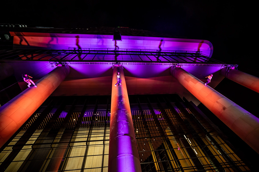 A building facade at night illuminated with vibrant purple and orange lights, creating an atmospheric and modern architectural display.