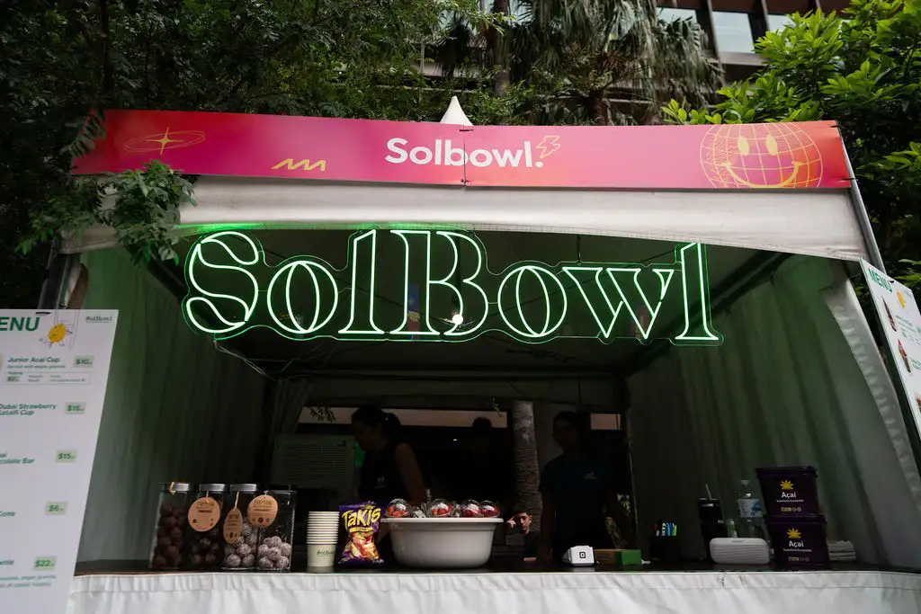 Outdoor food stall with a vibrant neon "SolBowl" sign. Menu items and snacks are displayed.