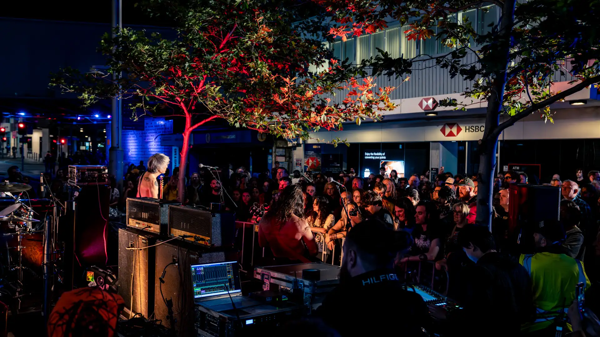 Outdoor concert scene at night with a vibrant crowd watching a band perform under a tree.
