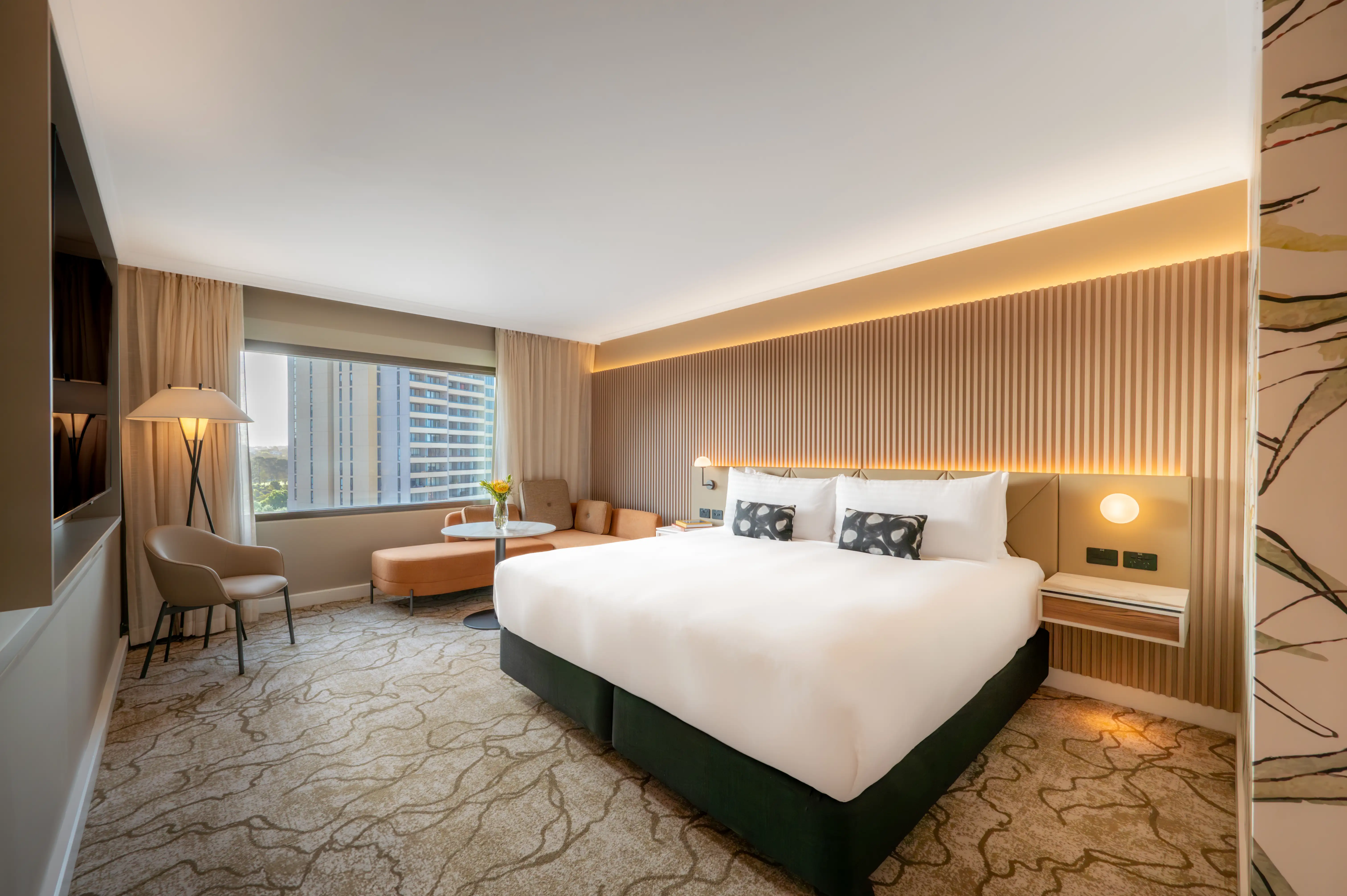 Modern hotel room with a large bed, elegant decor, and ambient lighting. A window shows a cityscape.