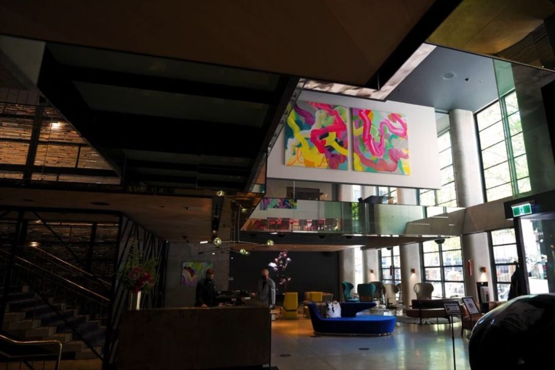 Spacious, modern hotel lobby with vibrant abstract art, large windows, contemporary furniture, and a reception desk; a calm, welcoming atmosphere.