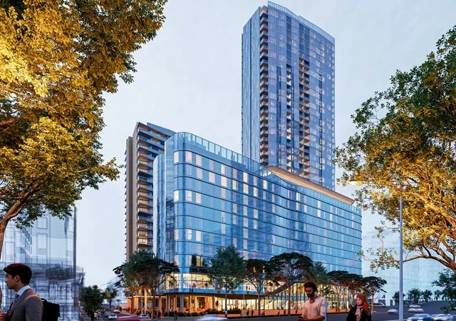 A modern glass high-rise building towers above a street lined with trees.