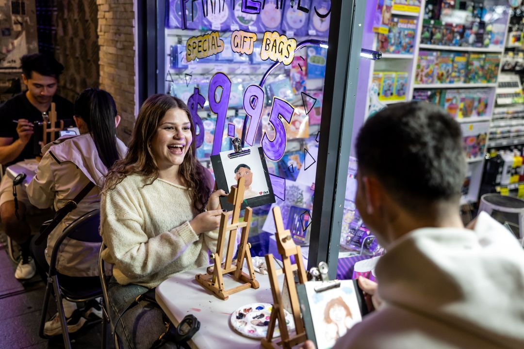 Girl sitting outside shop showing painting. 