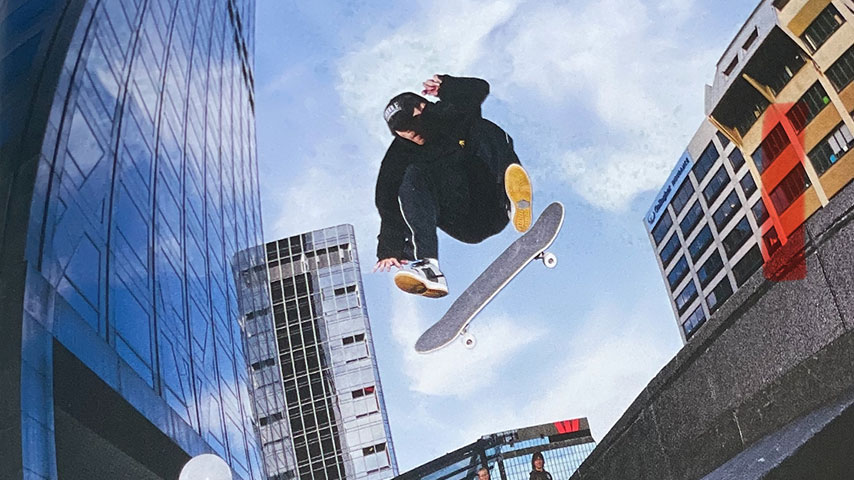 Skateboarder in black clothing leaps over a city ledge, board flipping beneath him, framed by tall glass buildings and blue sky.