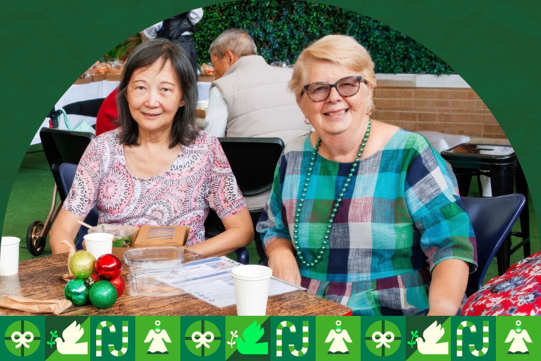 Two older adults seated together at a table during an indoor community event.