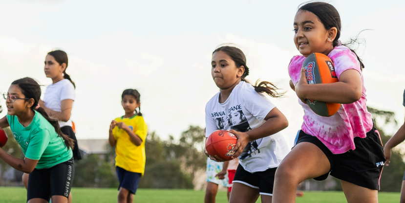 Girls running while holding a football in their arms and hands