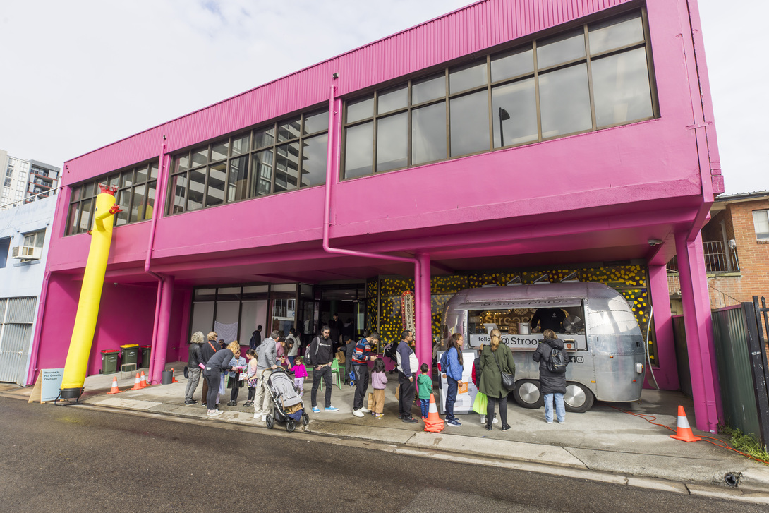 A group of people stands outside a pink building next to a silver truck parked on the street.