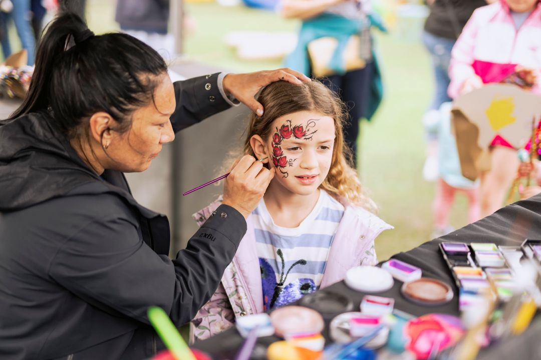 Woman face painting a little girl in the park