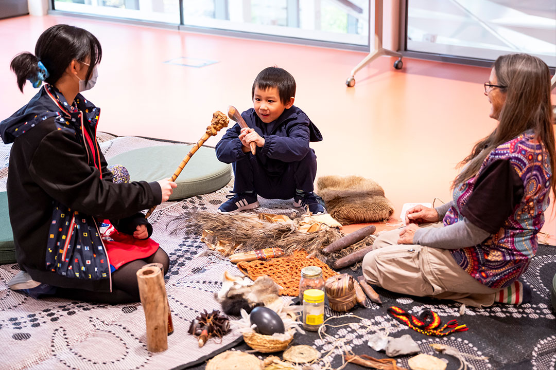 3 people sit in a circle looking at Aboriginal Artifacts