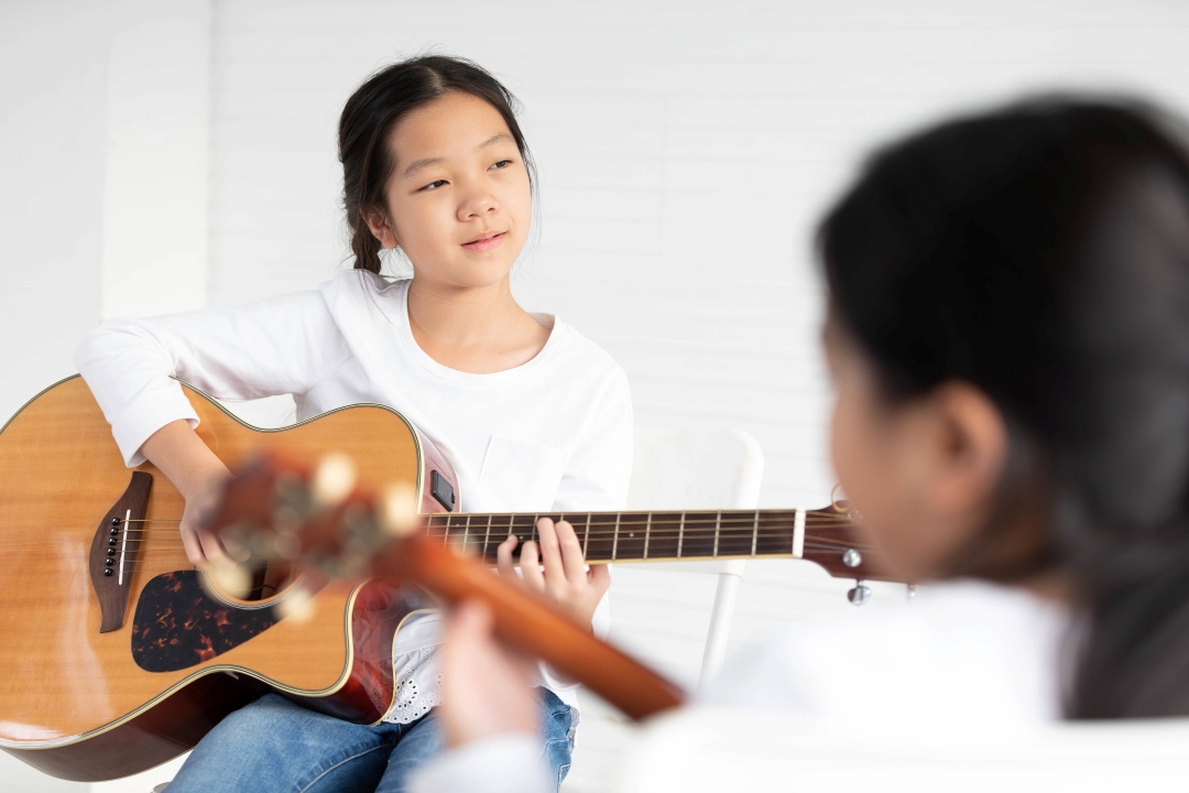 Girl holding guitar and wearing white long sleeve shirt
