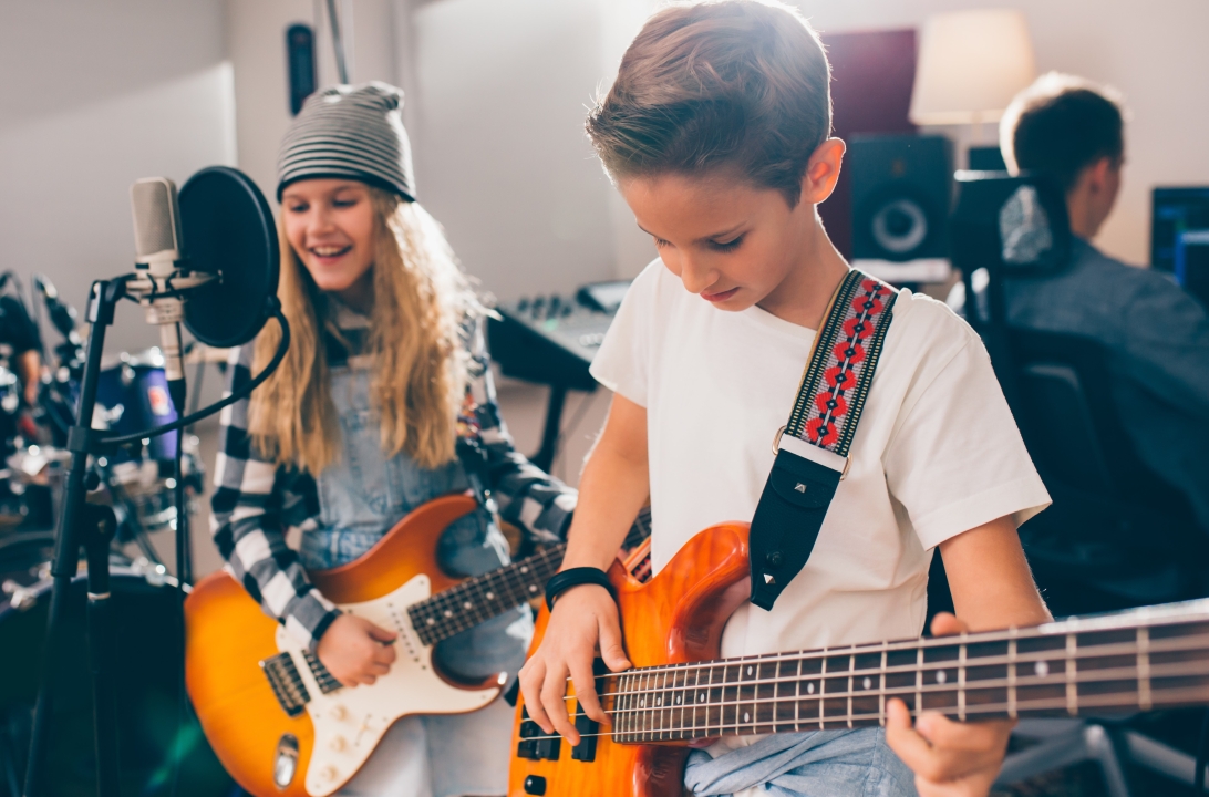 Girl and boy holding guitars standing behind microphones