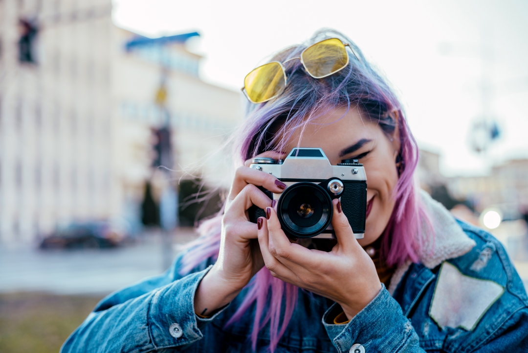 Woman with pink hair holding camera up to face