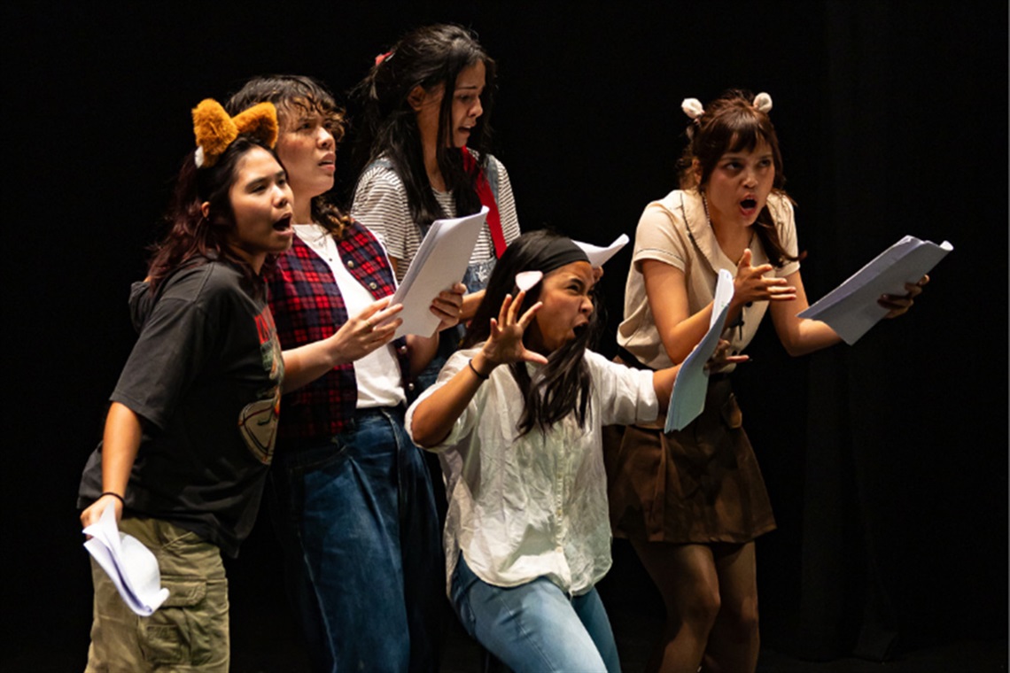 Five people on stage wear animal ear headbands and casual clothes, playfully posing with animated expressions. The scene is lively and theatrical.