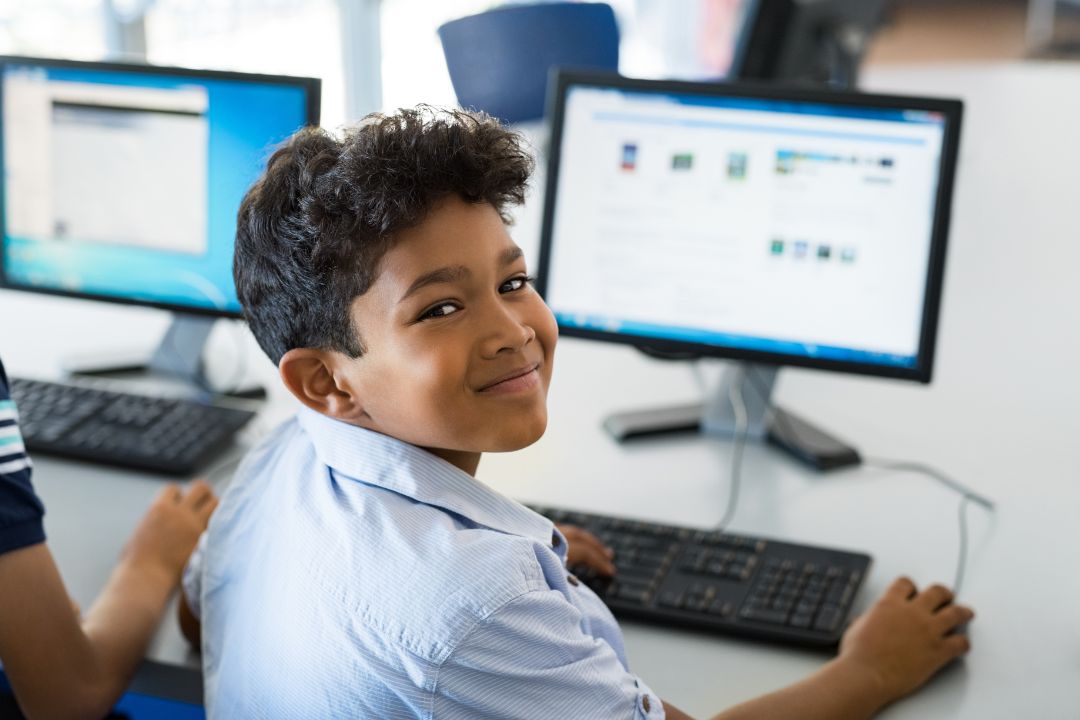 Young boy on a computer, looking over his shoulder to the camera