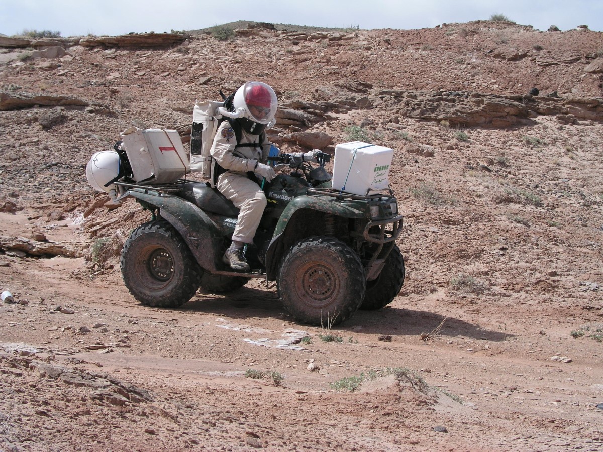 Person in space suit on a quad bike in the desert.