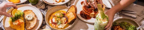 A table filled with tapas dishes includingQ olives, Spanish omelette, chorizo, and tomato salad. A hand reaches for food, creating a social and lively atmosphere.