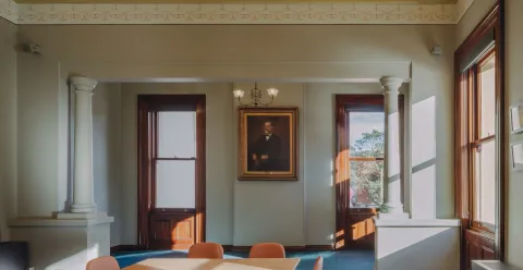 A room with a framed image with gold frame, and table and chairs in the centre of the room