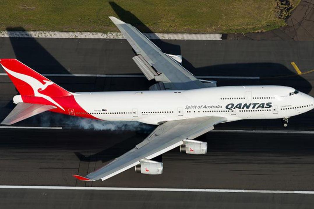 Image of Qantas 747 landing at Kingsford Smith International Airport Sydney. The plane is seen landing from above with smoke trails from the wheels as rubber burns at touchdown