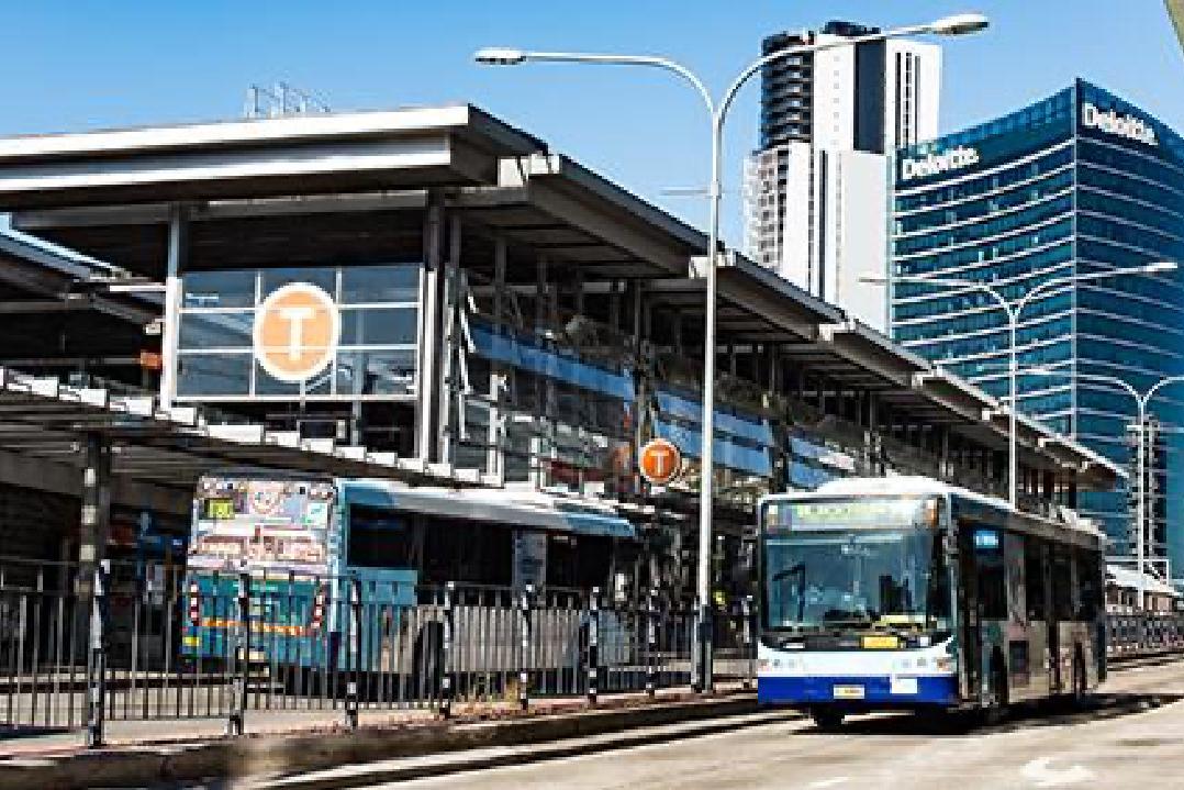 Image of the Parramatta bus transport interchange. Pictured are buses travelling in opposing directions and the indoor-outdoor glass station 