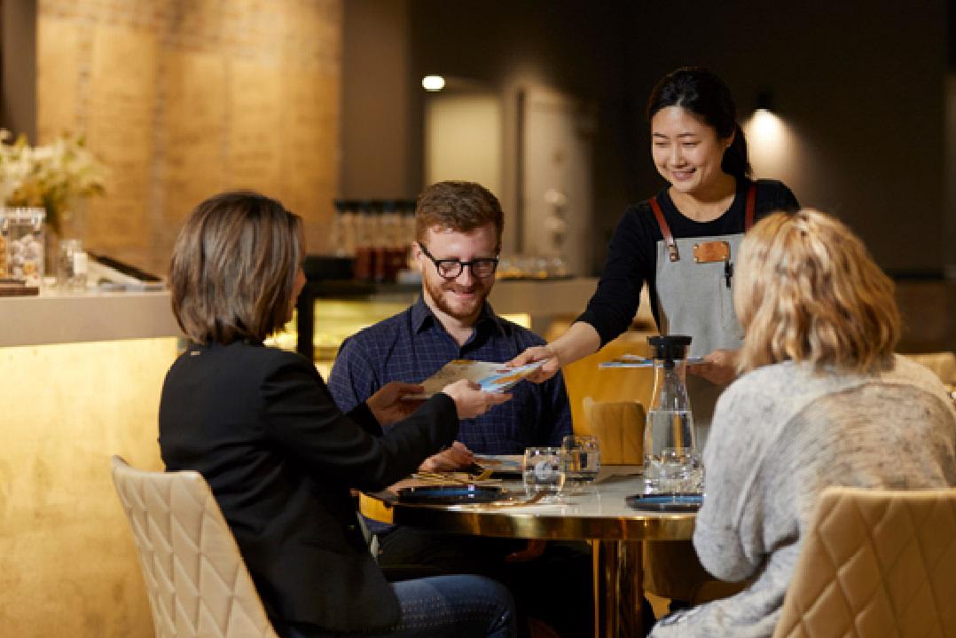 A hostess at an Italian restaurant hands out menus to a seated group of four