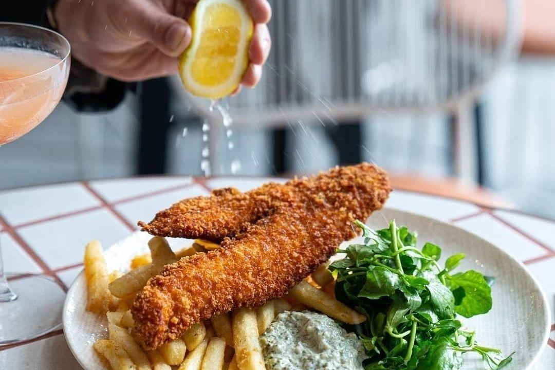 person squeezing a lemon onto fish and chips