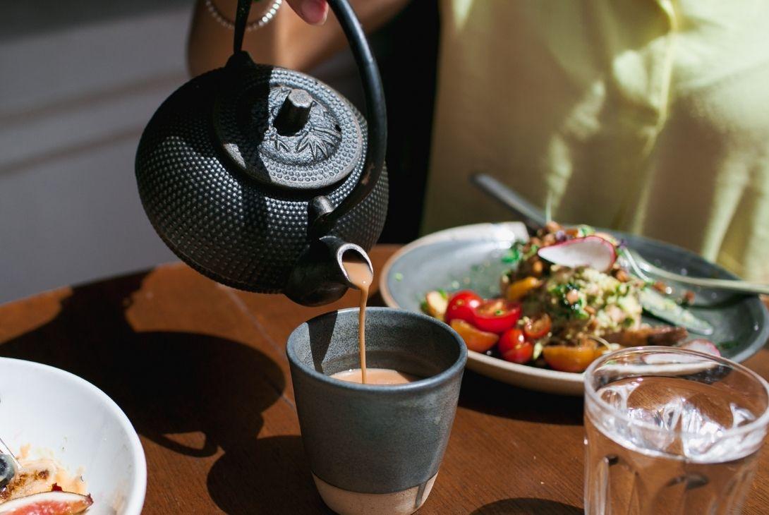 chai tea being poured with vegetarian food in the background