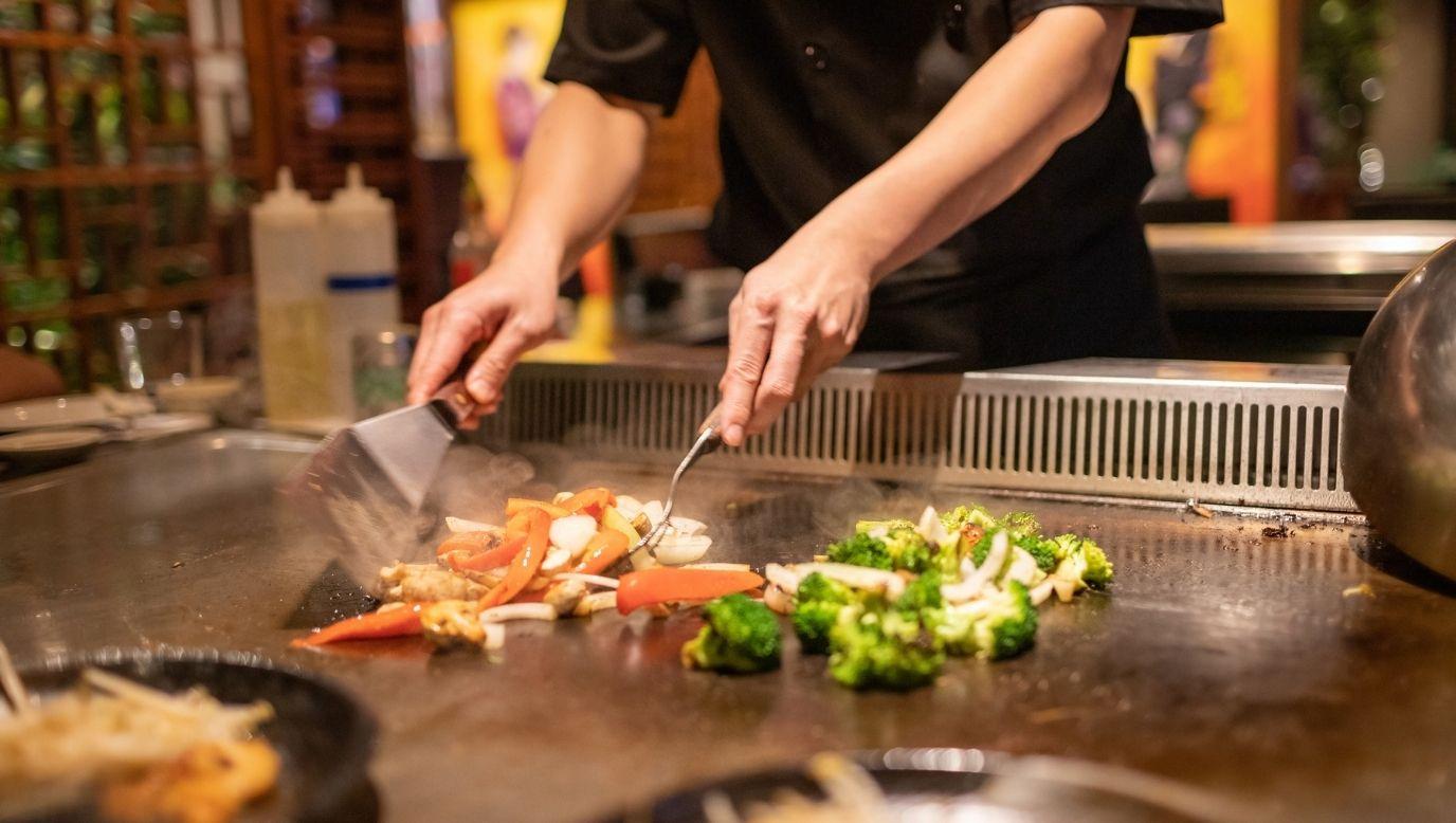 Teppanyaki chef cooking meat and vegetables over hot plate