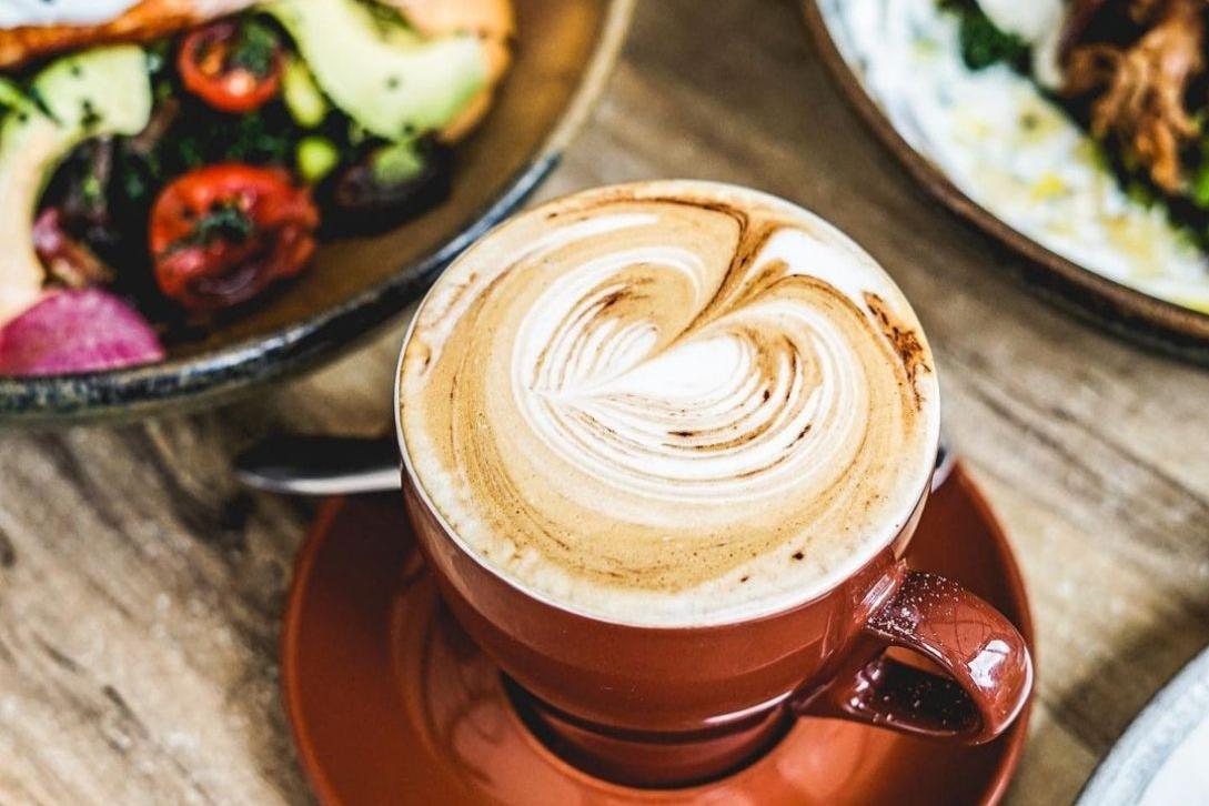 coffee in a coffee cup with food on plates next to it