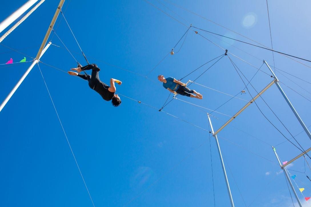two people practicising flying trapeze with blue sky background
