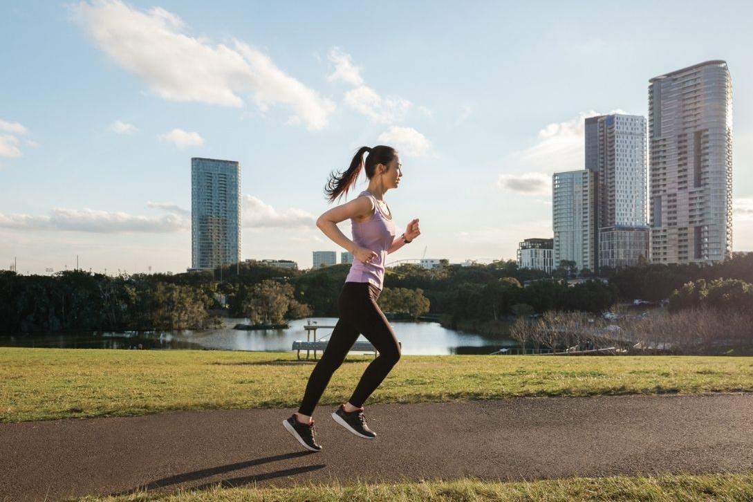 woman running on path next to river with skyscrapers in background